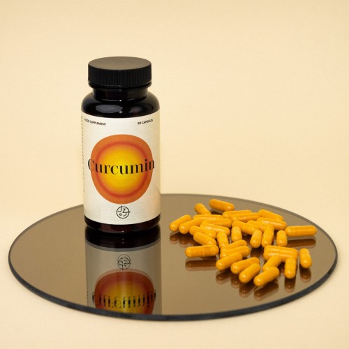 Curcumin -1.jpg Słoik z ciemnego materiału z kapsułkami Curcumin stoi na stoliczku, obok rozsypane kapsułki Curkumin. Oferta Jemy Zdrowo.